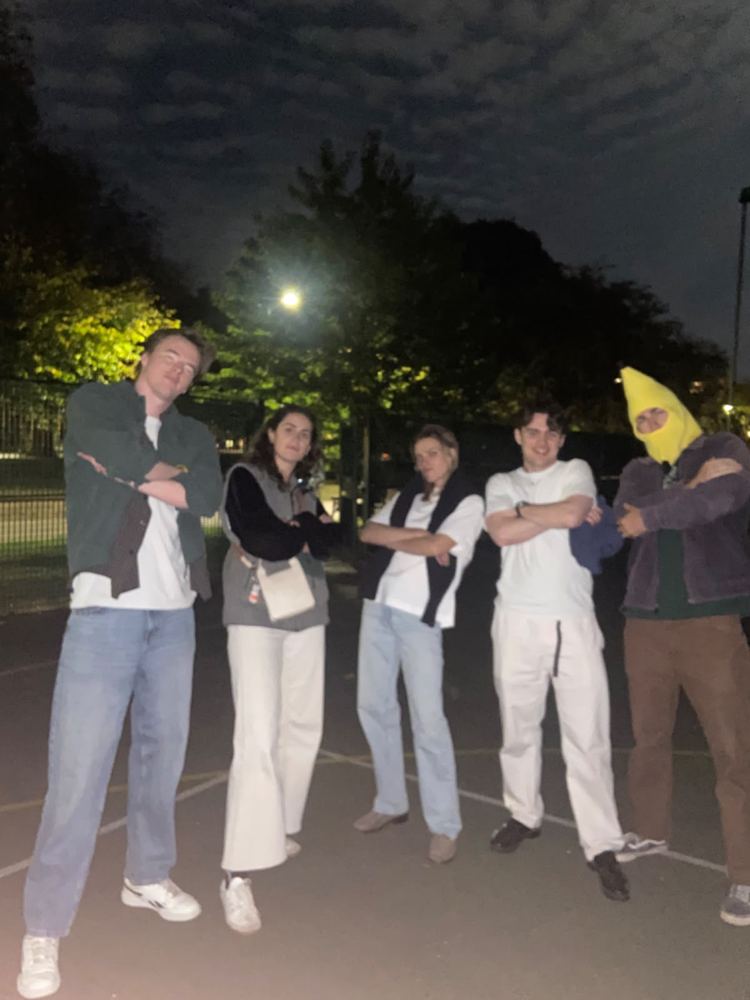 A crew striking an album-cover pose on a basketball court at night, one in a banana balaclava
