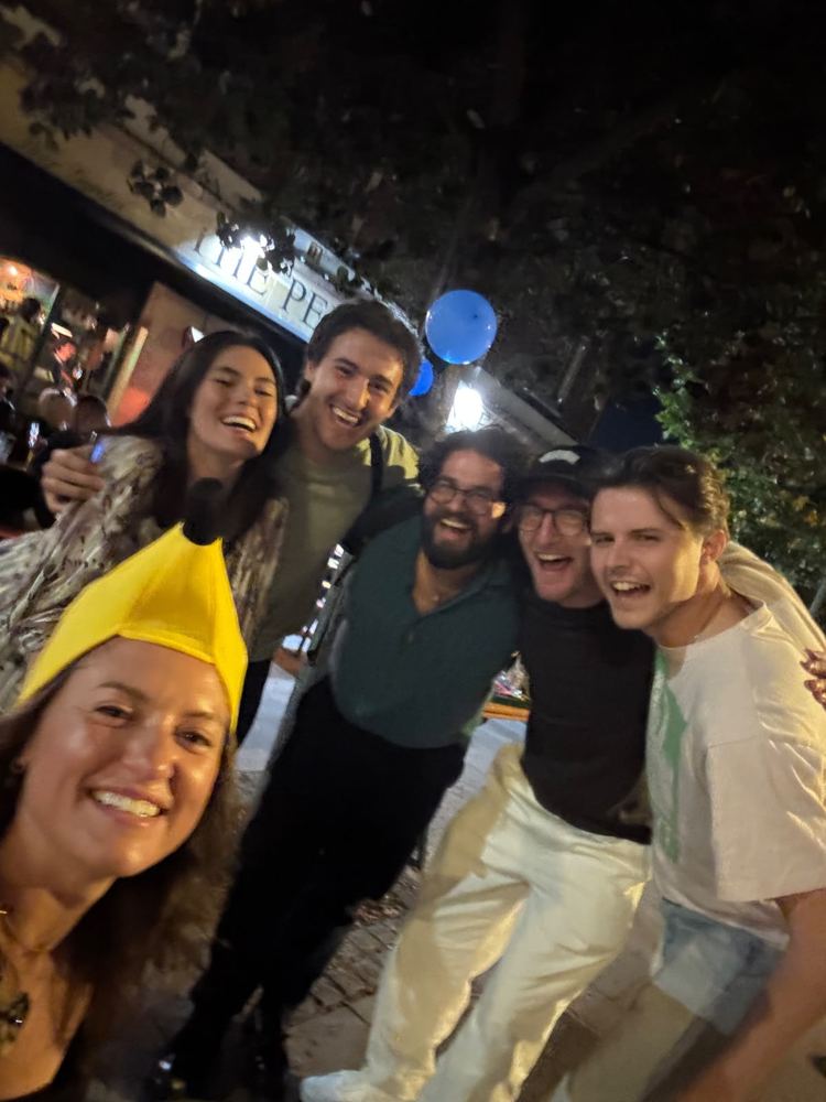 A crew grinning outside the pub at the finish line, captain in a banana hat